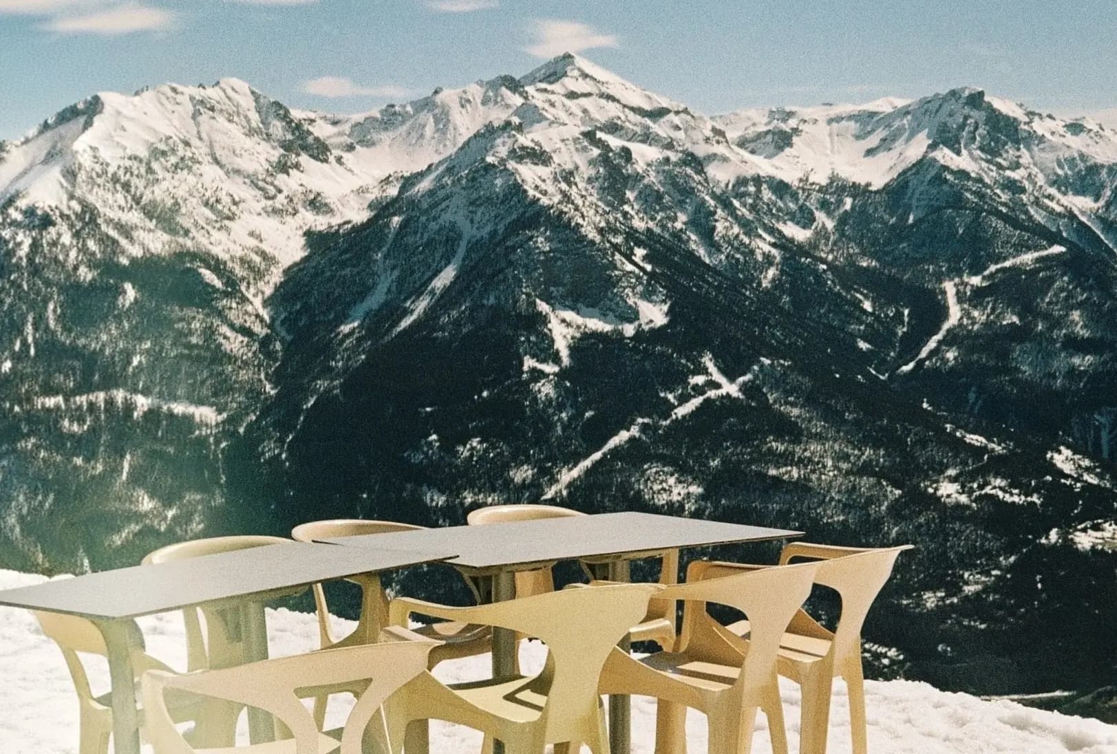 Section backdrop. An sunny image of the french alps. White plastic chairs and outdoor tables with a view of the snowy mountain range.